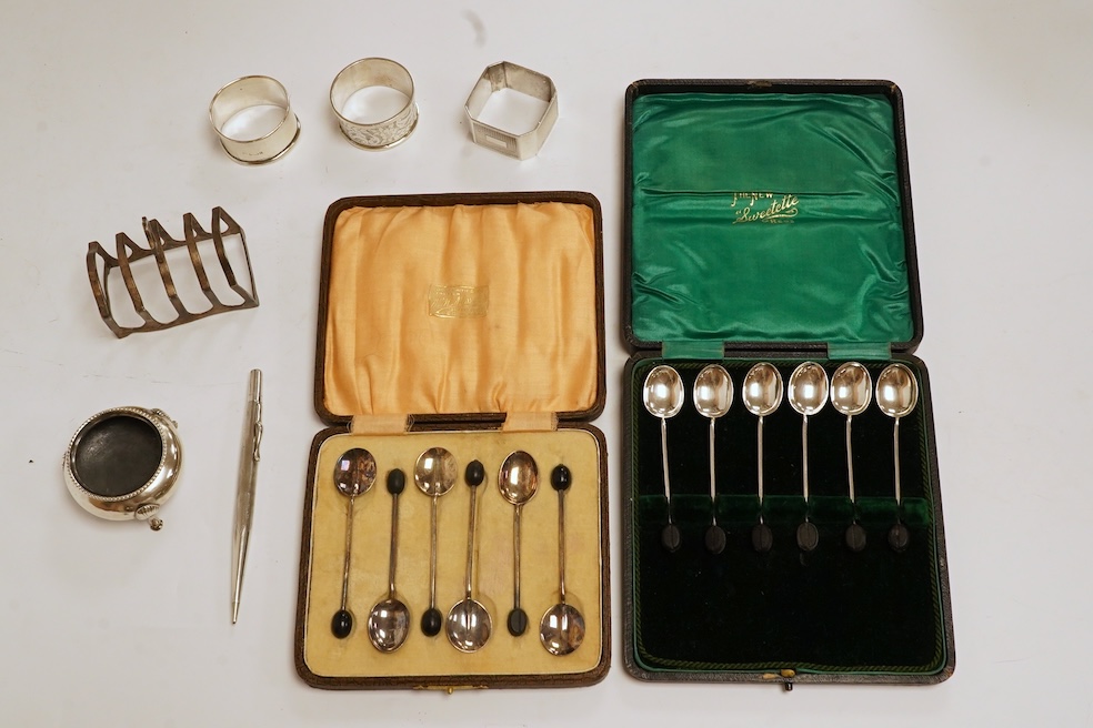 Two cased sets of six silver bean end coffee spoons, a Victorian silver bun salt, three assorted silver napkin rings, a small silver five bar toast rack and a sterling pen. Condition - poor to fair